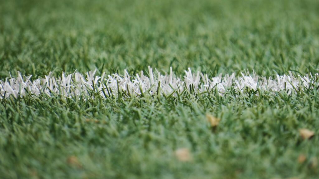 Detailed close-up of a white line on artificial green turf, perfect for sports backgrounds.